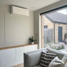 Interior fitted air con unit in neutral room, with grey chair and large window to outside