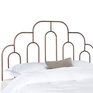 A dark brown metal headboard with an arched pattern on the border and within the frame, and white sheets and a gray throw pillow on the bed in front of it