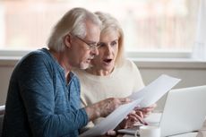 Concerned senior husband and wife hold documents using laptop checking information online, worried aged couple shocked by prices or tax growth reading bills on computer, man and woman have pc problem