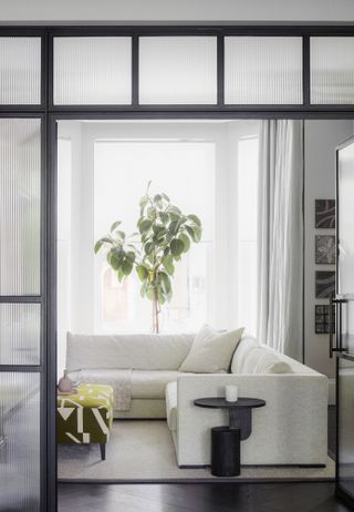 White corner sofa in a small living room with dark wood flooring and steel framed doors