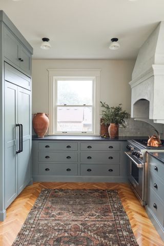 A blue kitchen with black hardware, a wooden floor with a rug laid on top and terracotta urns.