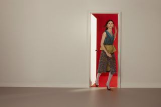 Model in colourful, eclectic outfit walks through a door to a red room wearing looks from the S/S 2025 season