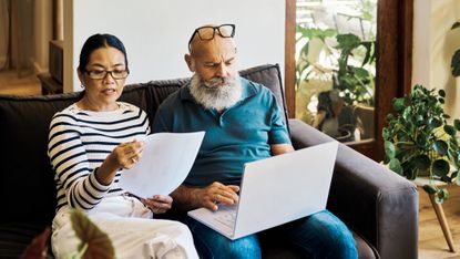 An older couple looking at financial paperwork and paying bills on a laptop