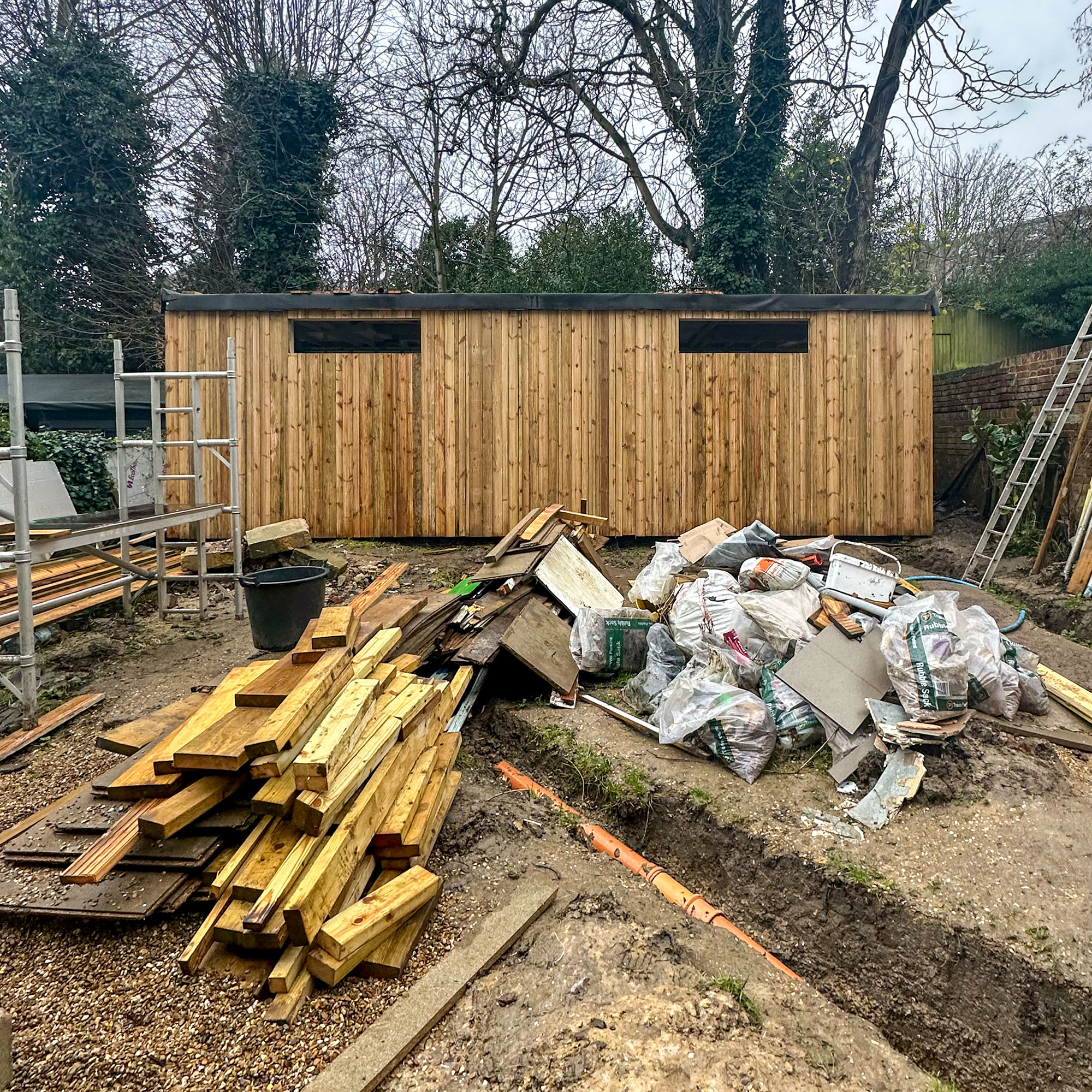 Garden dug up mid-renovation with piles of wood and building materials in front of wooden garden room