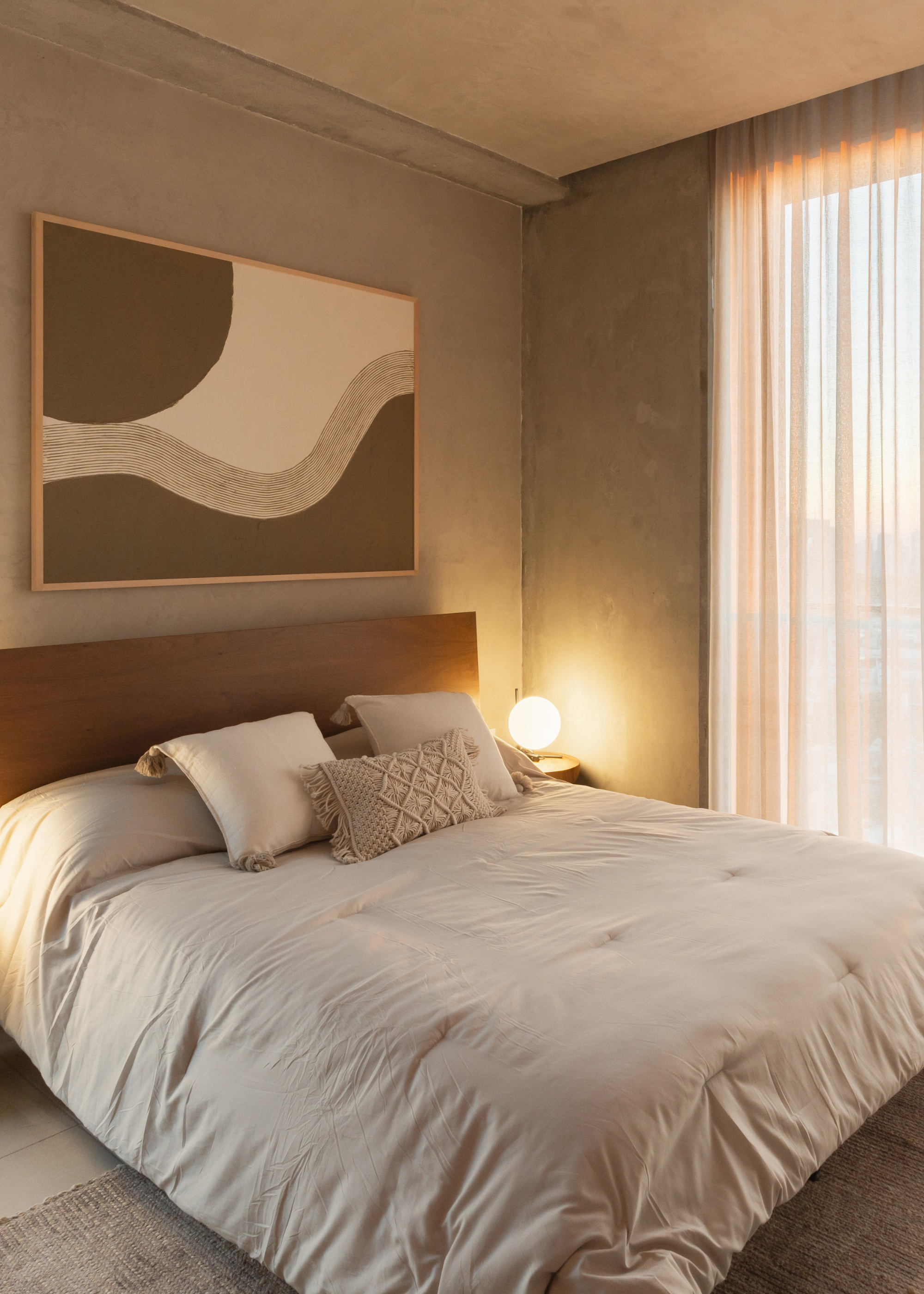 A beige bedroom with framed art, a wood headboard, a light bedscape, and throw pillows