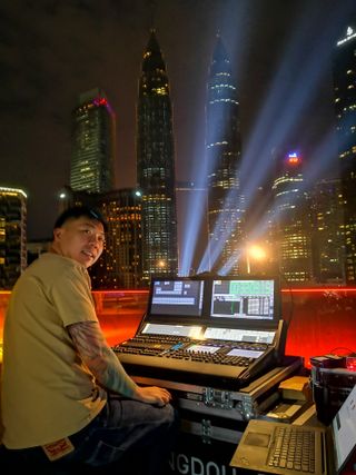 A lighting engineer smiling at his console as lights beam up on a building.