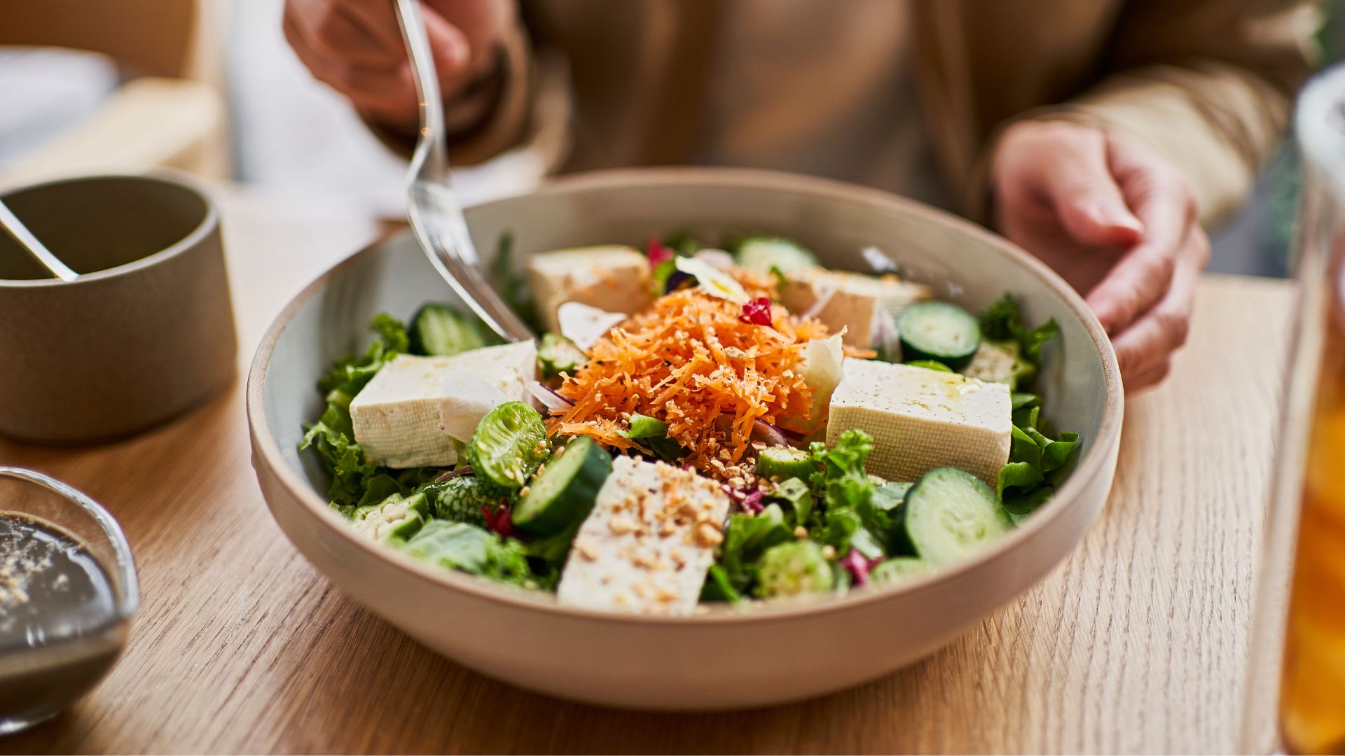 Woman eating a bowl of salad with tofu or tempeh in the middle, representing the benefits of a vegan diet for menopause