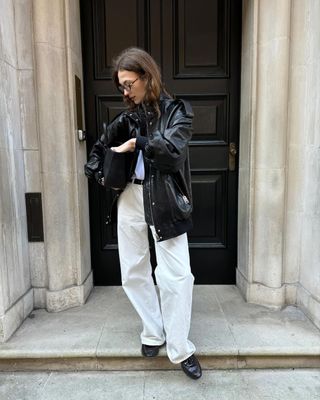 fashion influencer @oliviasshoppingdiary wearing a leather bomber jacket with white jeans and black loafers