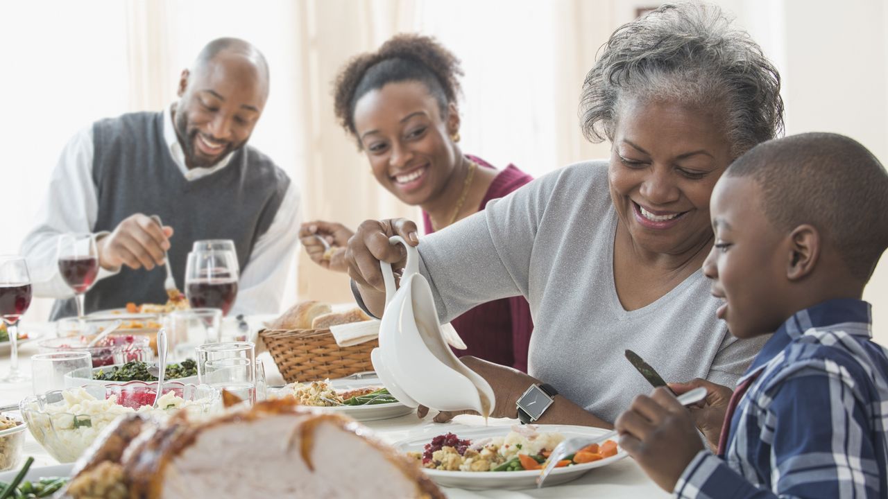 A grandma pours gravy on her grandson&#039;s turkey during Thanksgiving dinner with the family. 