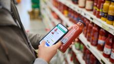 Man checking price of tomato sauce on smartphone in supermarket