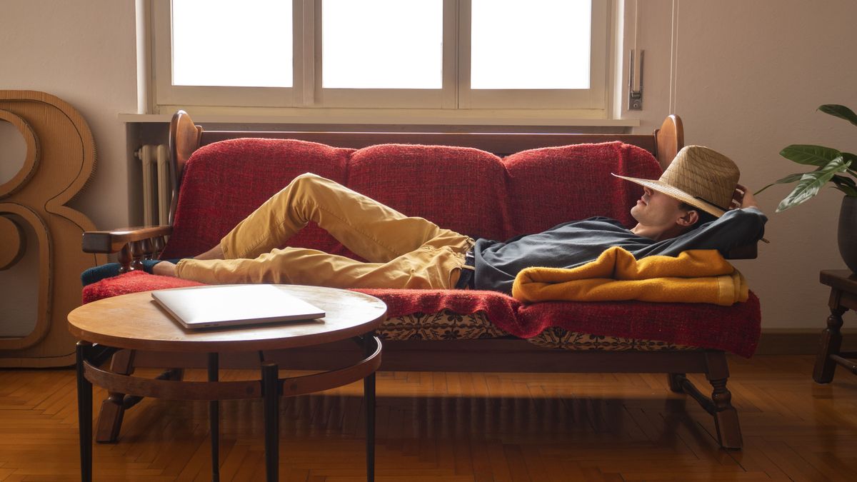 A man relaxing on a couch with a laptop on a nearby coffee table