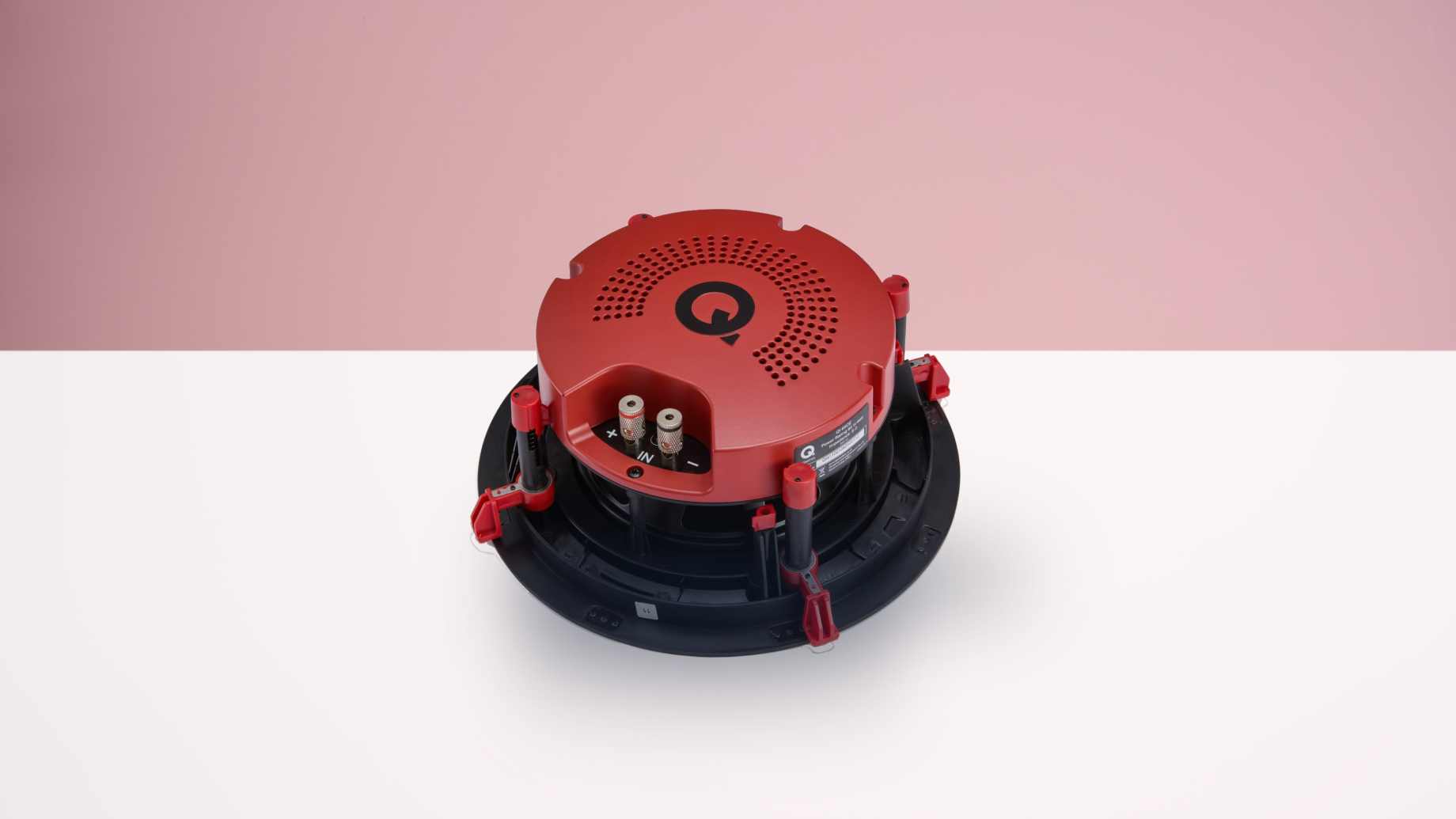 The Q Acoustics QI65CE on a white surface before a pink background.