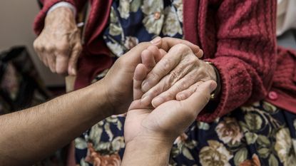 A pair of younger hands grasp the hand of an elderly woman.