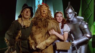 Dorothy, the Tin Man, the Scarecrow, and the Lion look at something off-screen in The Wizard of Oz