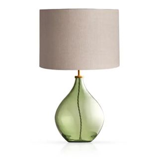 A table lamp with a green glass base and a beige shade