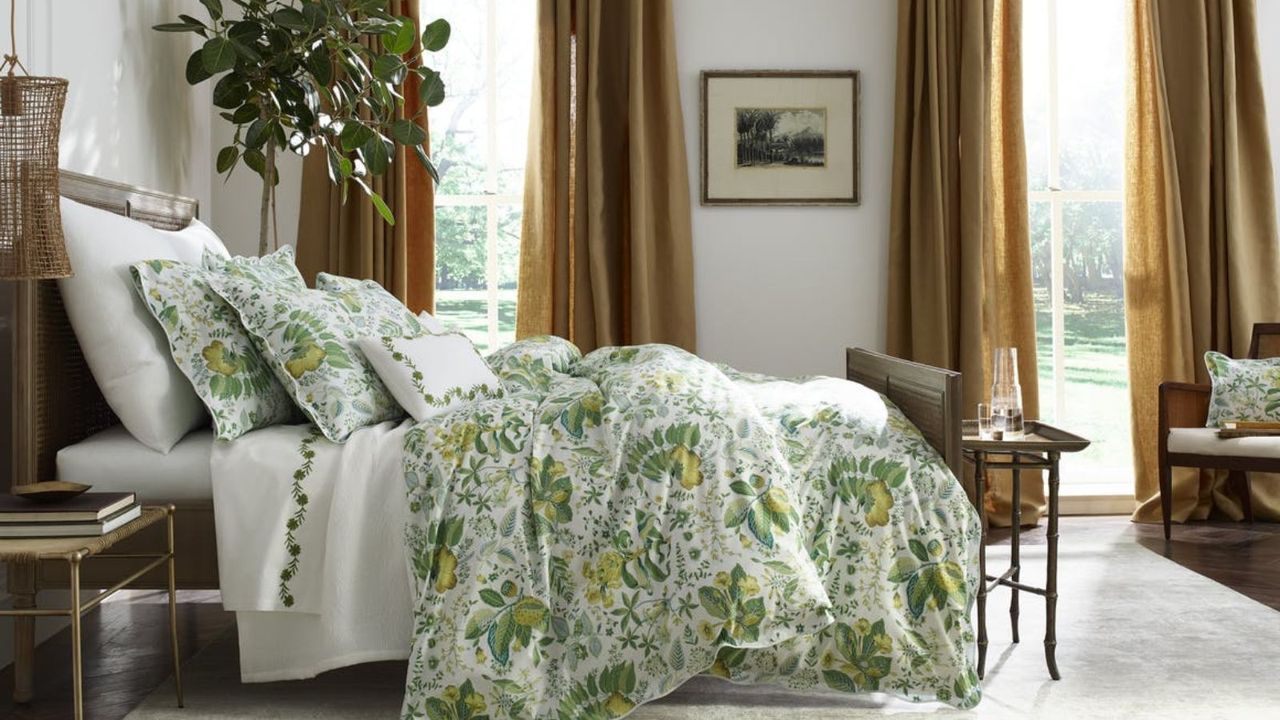 Side view of green and white bedding on a bed against white walls and brown curtains. 