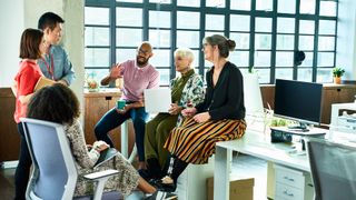 Soft skills concept image showing informal staff meeting in an open plan office environment with workers having a discussion.