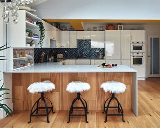 A contemporary wood and white gloss kitchen with kitchen island and bar stools with faux fur chair decor