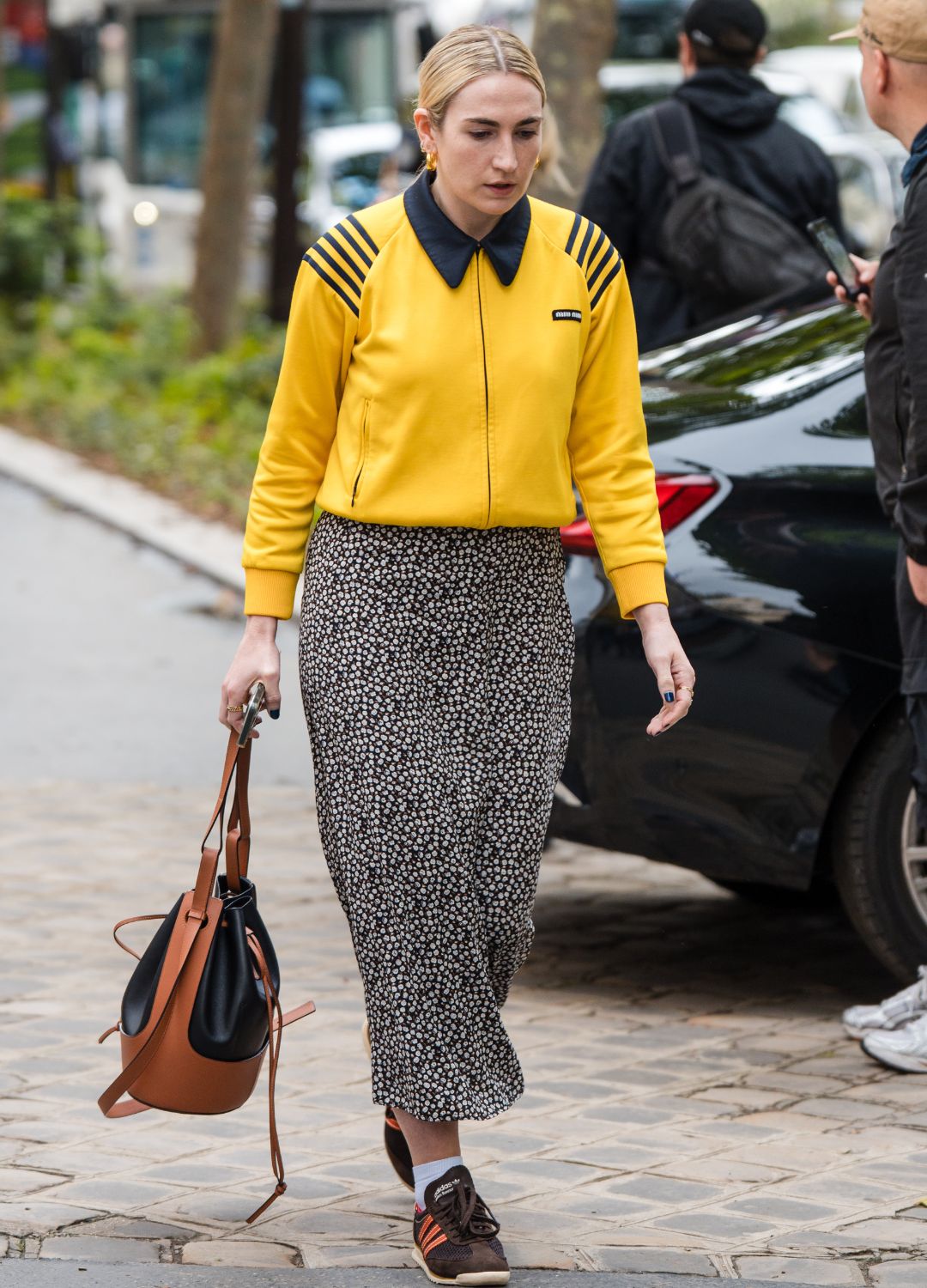 A guest wears yellow Miu Miu jacket with black details, black and white floral print midi skirt, brown Adidas sneakers, brown bag, outside Loewe, during the Haute Menswear Spring/Summer 2025 as part of Paris Fashion Week on June 22, 2024 in Paris, France