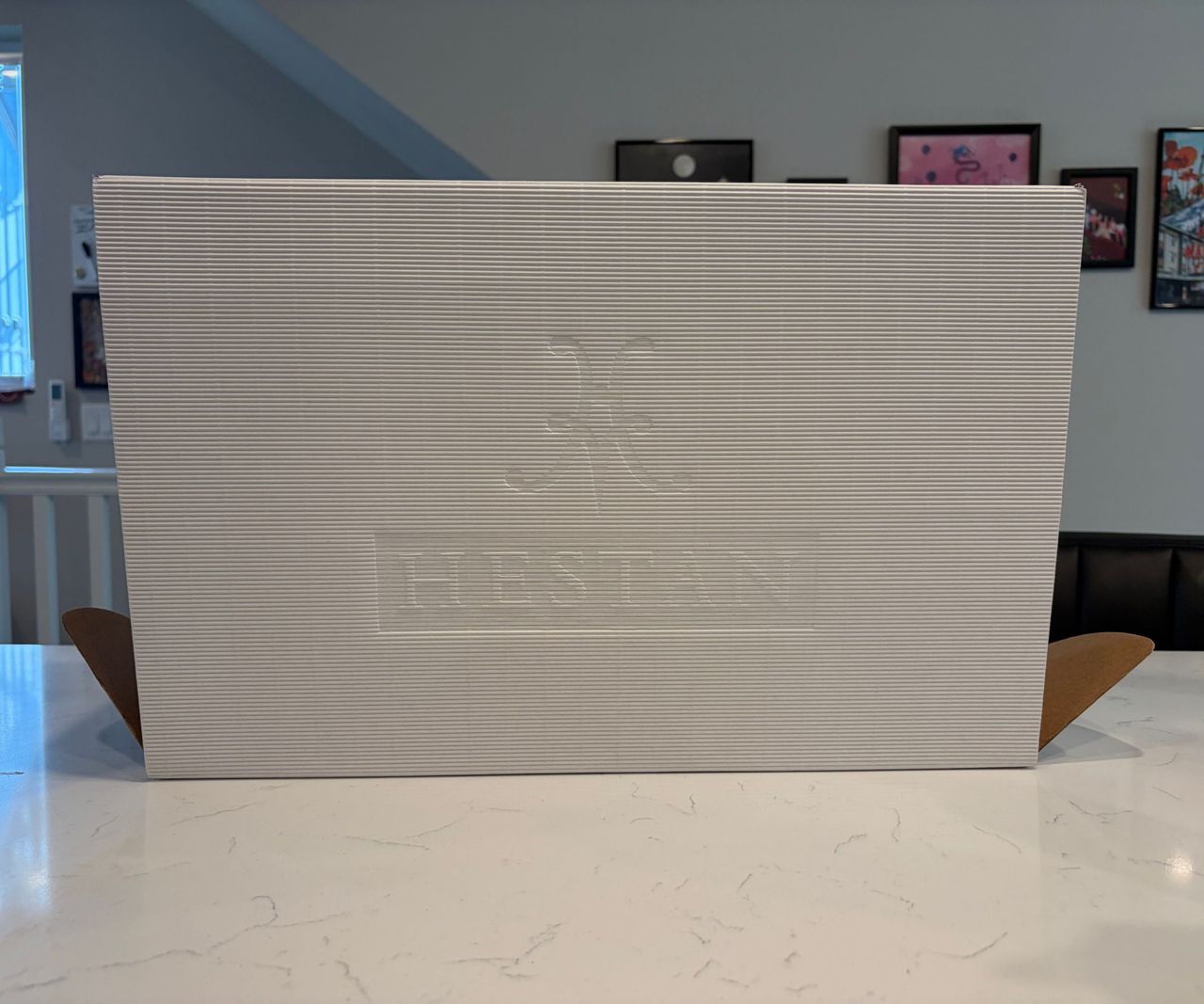 A white cardboard box with the Hestan branding debossed on the side, on a white kitchen counter
