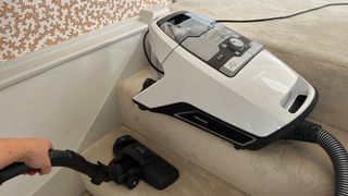 Miele Blizzard CX1 canister vacuum on a step while tester cleans the stairs below