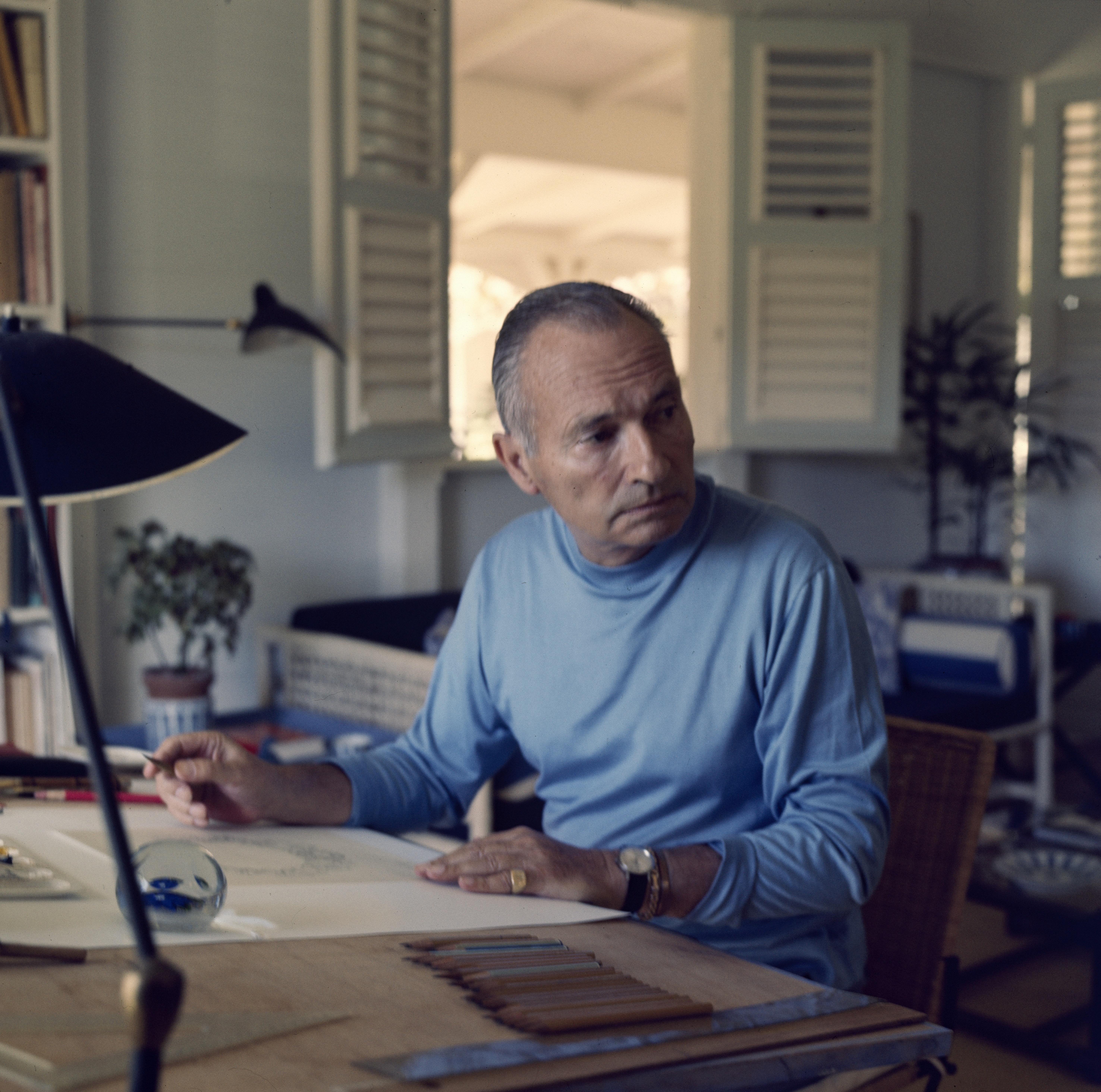 Jean Schlumberger in a blue polo neck working at a drawing desk