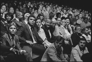 Black and white photo of Mohammed Ali sitting in a crowd.