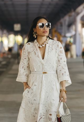 A New York Fashion Week guest wears an ivory conch shell necklace and a white lace dress