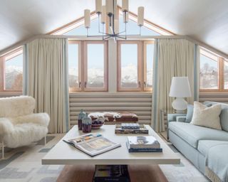 A bright room with a wide coffee table, blue sofa, white fluffy chair, curtains and a statement light