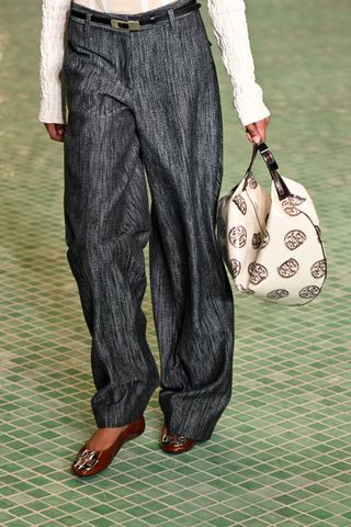 A model wears Tory Burch ballet flats on the runway with trousers.