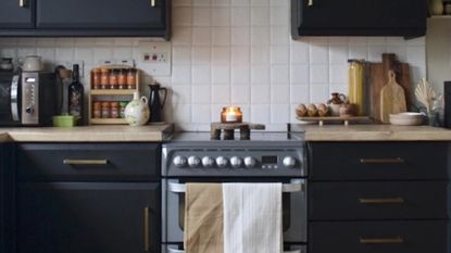 kitchen with dark painted cabinets, painted tiles and an oven with tea towel