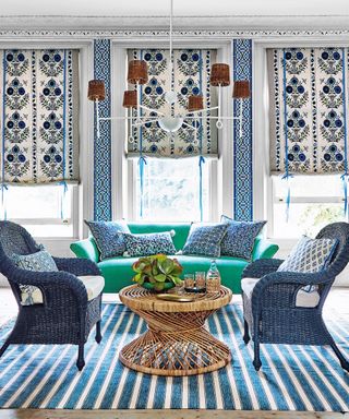 A living room with blue and white soft furnishings, blue armchairs, green sofa, and low hanging chandelier