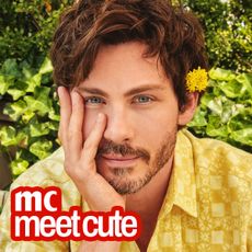 logan lerman wears a yellow flower in his ear and a yellow shirt and holds his chin in his hand 