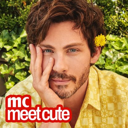 logan lerman wears a yellow flower in his ear and a yellow shirt and holds his chin in his hand