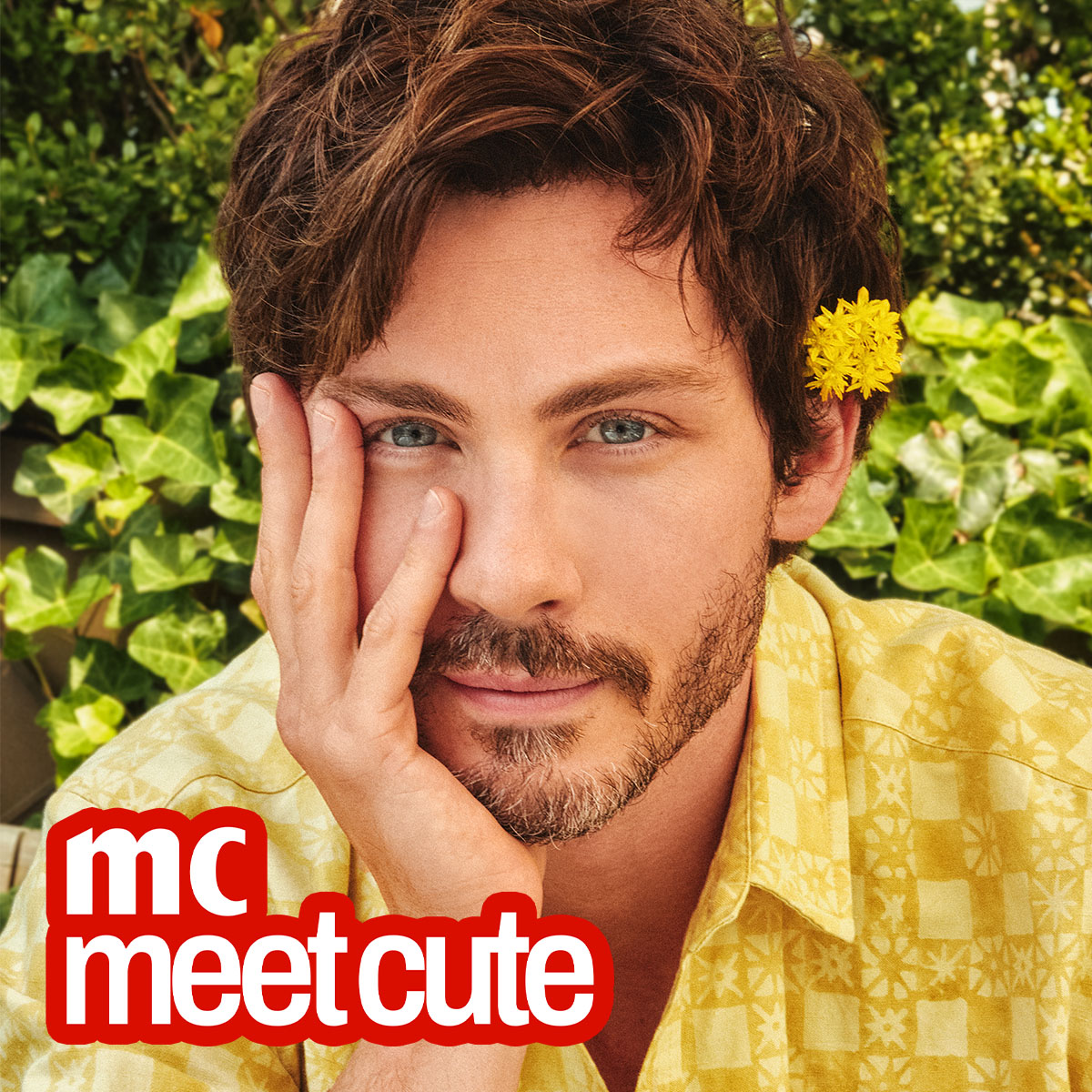 logan lerman wears a yellow flower in his ear and a yellow shirt and holds his chin in his hand 