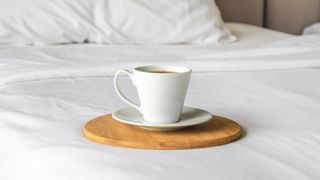 A cup of coffee on a wooden board, sat on a white bed