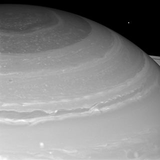 Saturn and its north polar hexagon dwarf Mimas as the moon peeks over the planet's limb. Saturn's A ring also makes an appearance on the far right. Image released March 18, 2013.