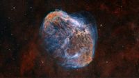 A red and blue nebula glows against distant stars. A bright blue star can be seen glowing in its core.