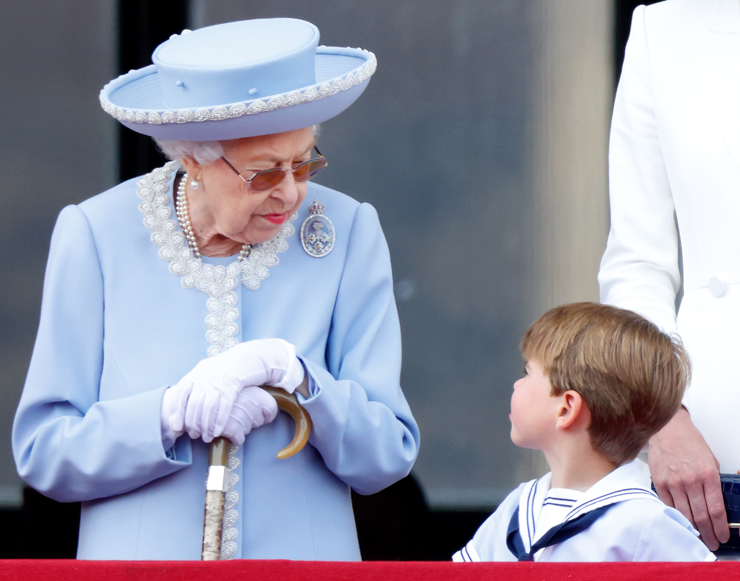 Queen Elizabeth wearing a blue coat and hat looking down at Prince Louis