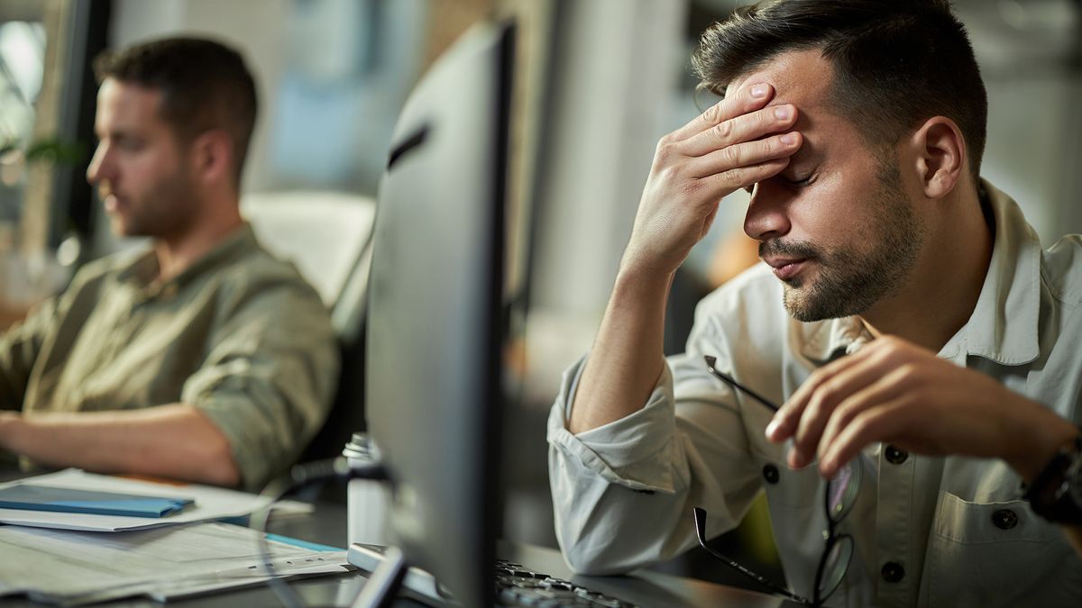 Two IT workers looking stressed at their desk. One is massaging his forehead with his right hand