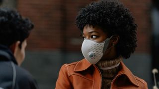 A woman with dark hair and an orange jacket wears the AirPop Active+, in white, while out in New York City during the coronavirus pandemic
