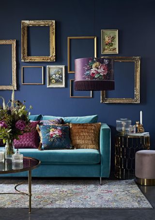 Blue living room with turquoise blue couch, vintage rug, floral cushions, vintage frames on the wall, fringed floral pendant light, gold coffee table, side table, footstool, flowers