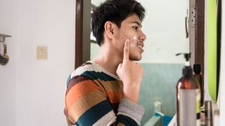 man applying cream to his acne in the mirror