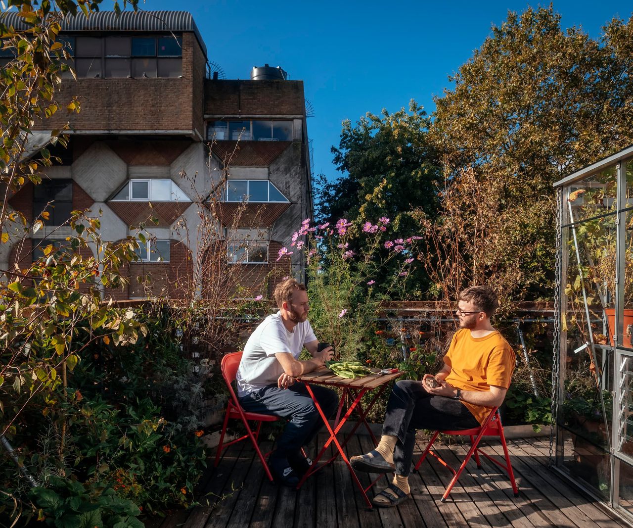 A rooftop terrace with flower beds and a greenhouse and sitting area