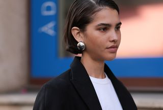 Guest is seen outside The Row show wearing silver earrings, black blazer, white shirt underneath, black pants with wide leg and cutouts, red lace-up heels, and a Gucci Jackie in brown with Gucci monogram during Paris Fashion Week on September 27, 2023 in Paris, France.