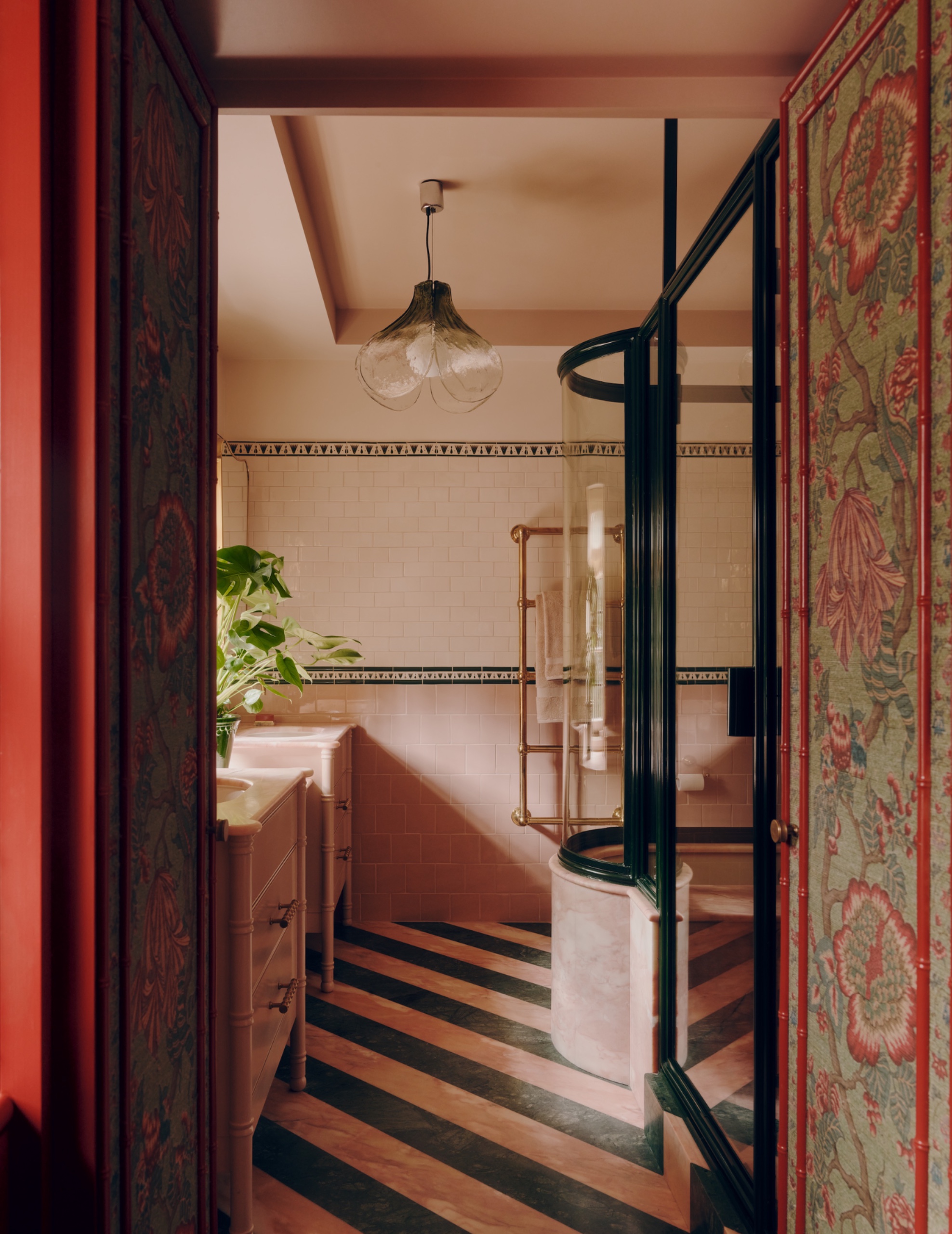 Bathroom with diagonal pink and green marble floor stripes, pink and cream wall tiles, and a curved bath enclosure framed in dark green.