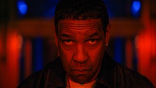 Denzel Washington in a still from Highest 2 Lowest. He fills the frame and is lit in red light; the background behind him is blurry but is also red with blue highlights. He doesn't look very happy
