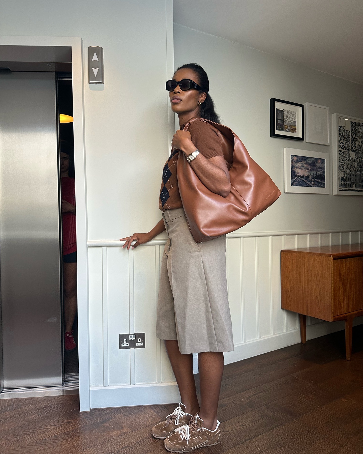 @nlmarilyn wearing a brown oversized shoulder bag, argyle Miu Miu sweater, long tan culotte shorts, and Miu Miu suede sneakers.
