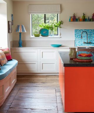A colorful beige, pale blue and red kitchen in a country home in Sussex designed by Kate Forman, with orange-red kitchen island and wooden flooring.