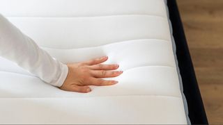 Hand pushing into a white mattress to show body impression.